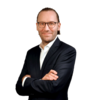 Mann mit Brille im dunklen Anzug, lächelnd mit verschränkten Armen vor schwarzem Hintergrund